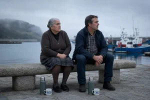 Una abuela gallega y un señor de mediana edad sentados juntos en un banco de granito frente al puerto de Cariño, los dos con la misma expresión melancólica, niebla suave sobre el mar y un termo a sus pies
